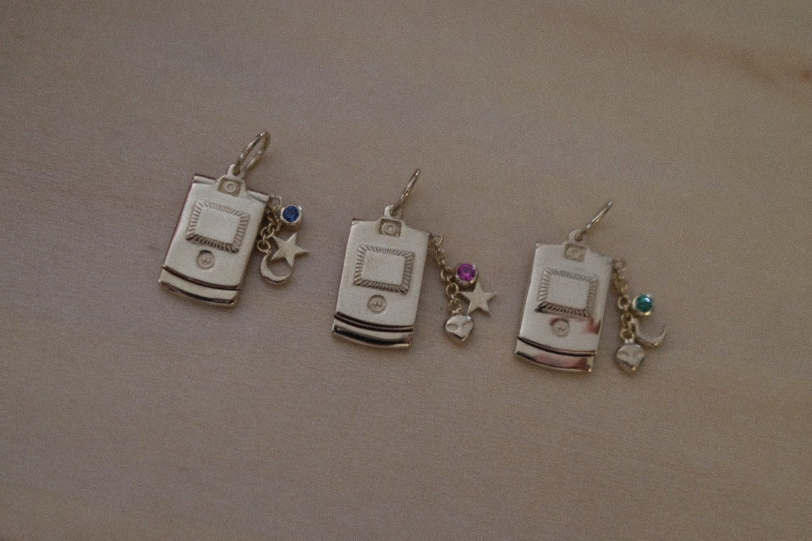 Three small silver charms resembling vintage cell phones on a wooden surface.