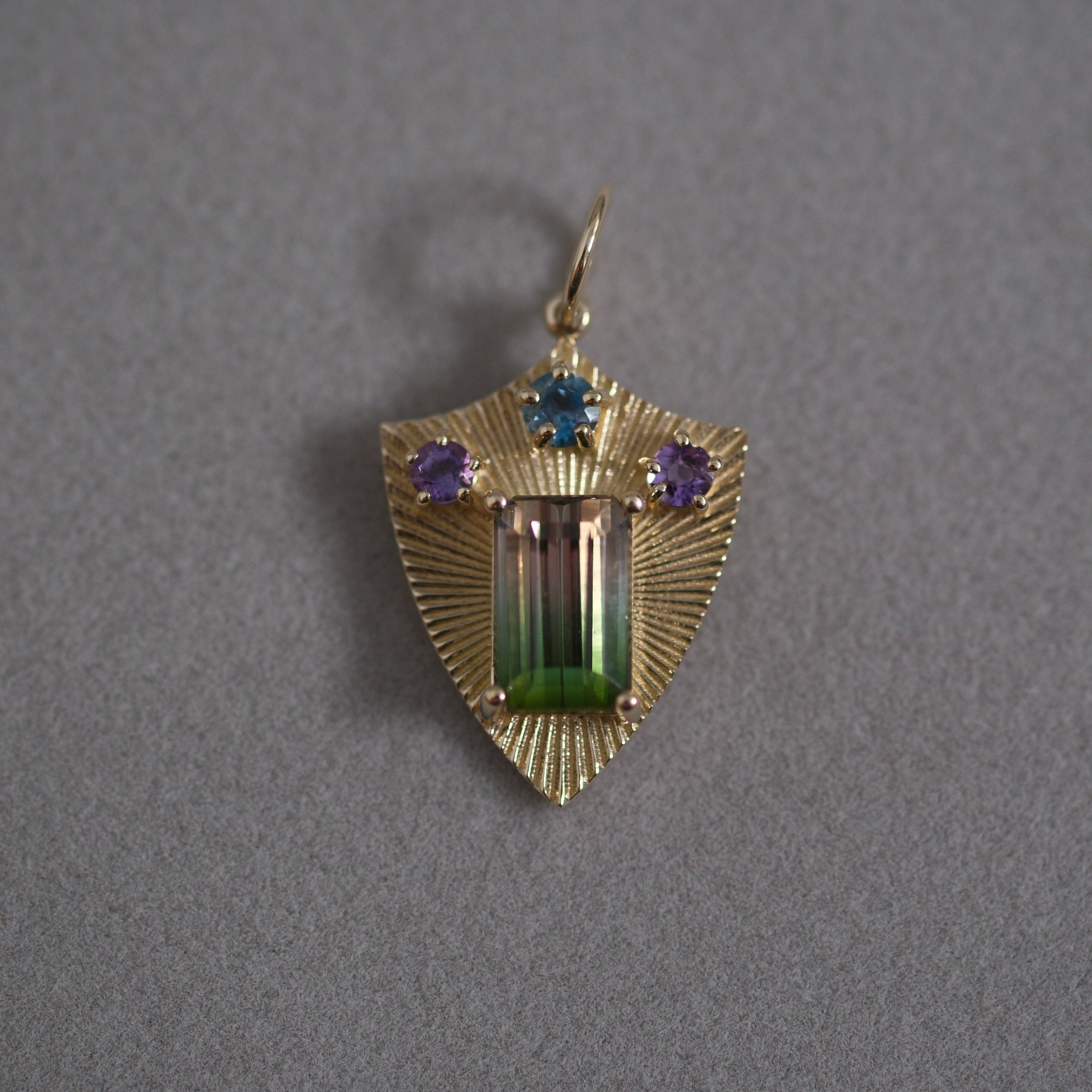 Gold pendant with bi-color tourmaline, aquamarine, and amethyst gemstones on a gray background